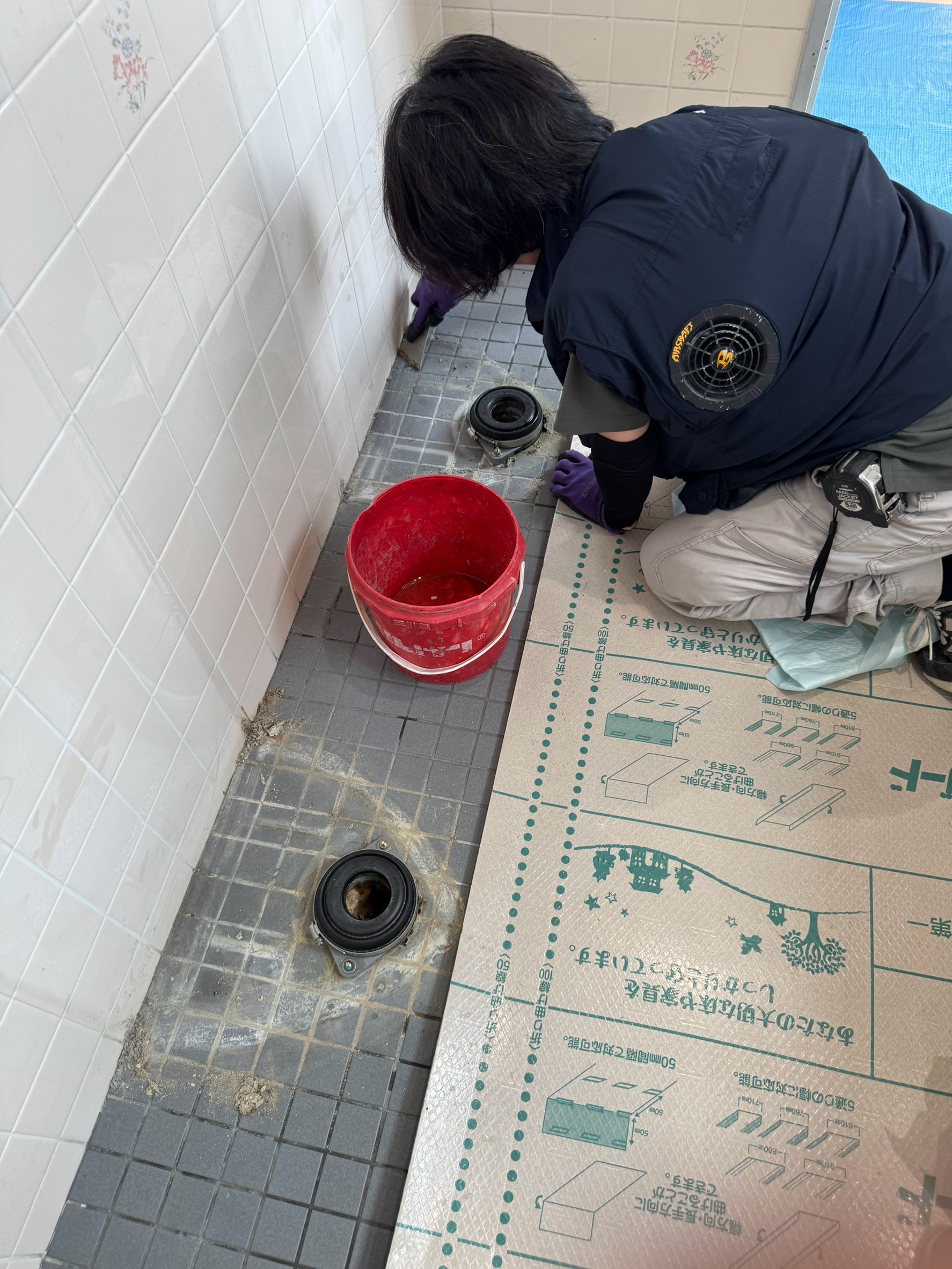 小便器の取付前に排水金具まわりの床を清掃する様子。下地を整える施工中の作業（神戸市東灘区・施工中）